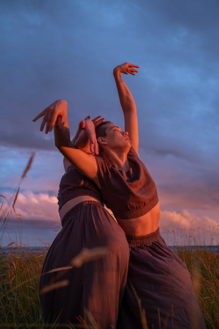 Two women gracefully dancing in a grassy field at sunset.