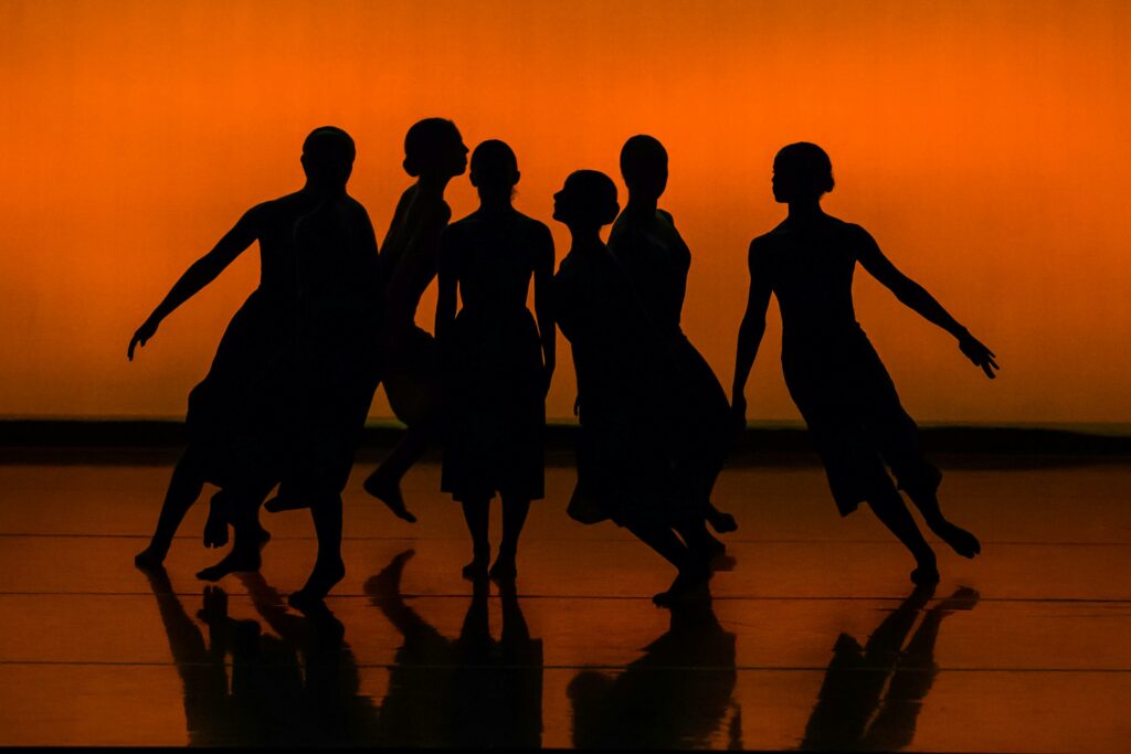 Silhouetted dancers performing contemporary ballet in dramatic lighting.